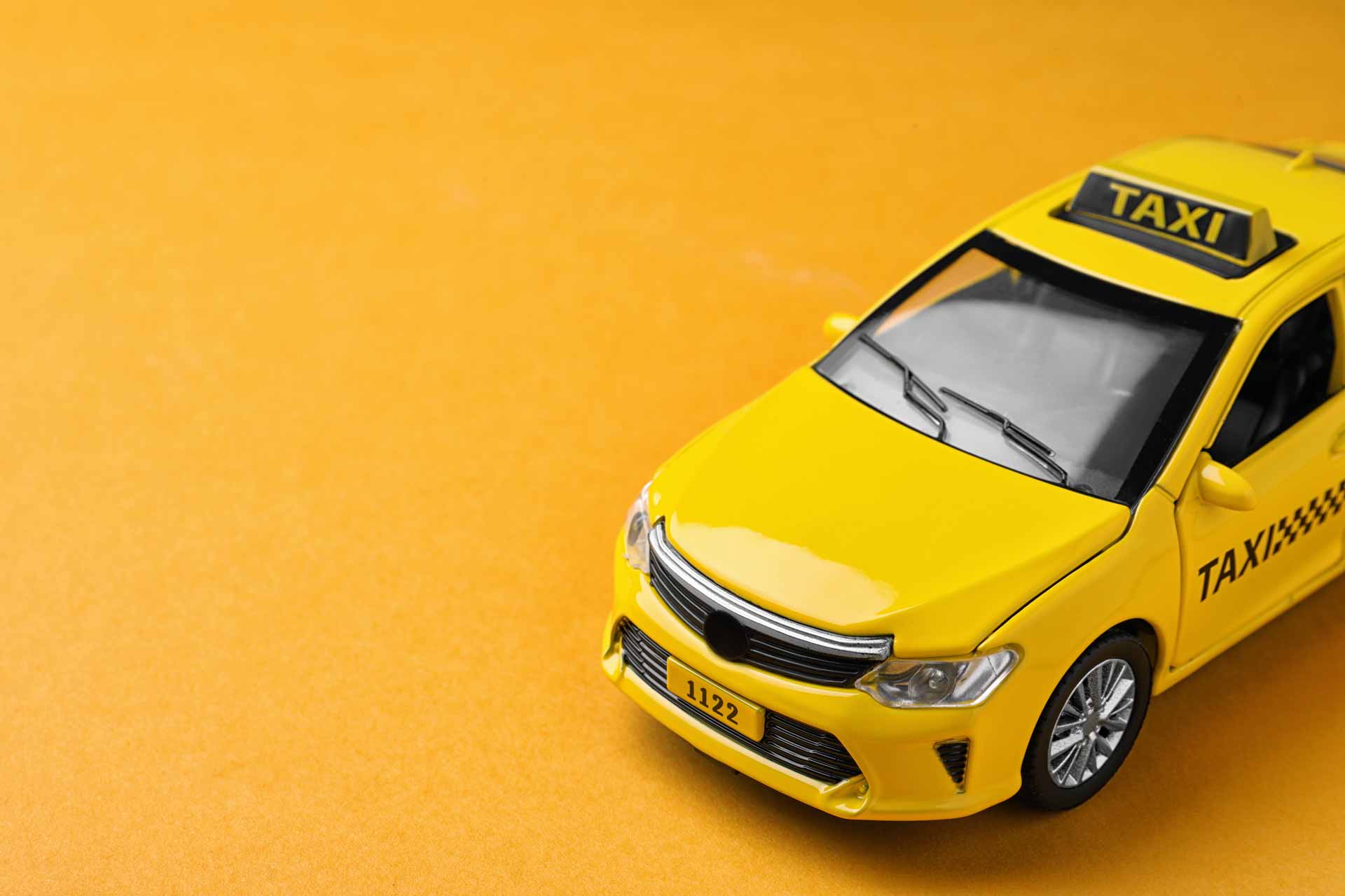Toy taxi cab on solid yellow background